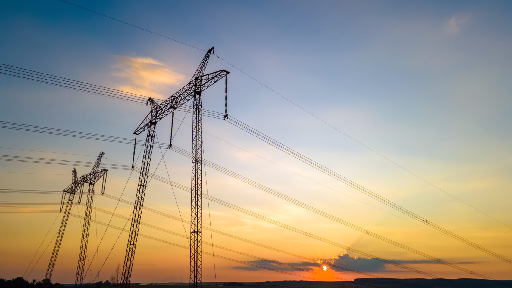Dark silhouette of high voltage towers with electric power lines at sunrise.