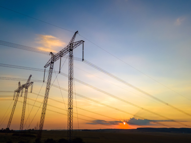 Dark silhouette of high voltage towers with electric power lines at sunrise.